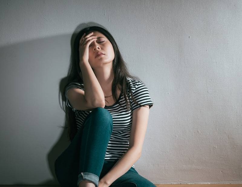 An upset woman sitting on the floor looking sad.